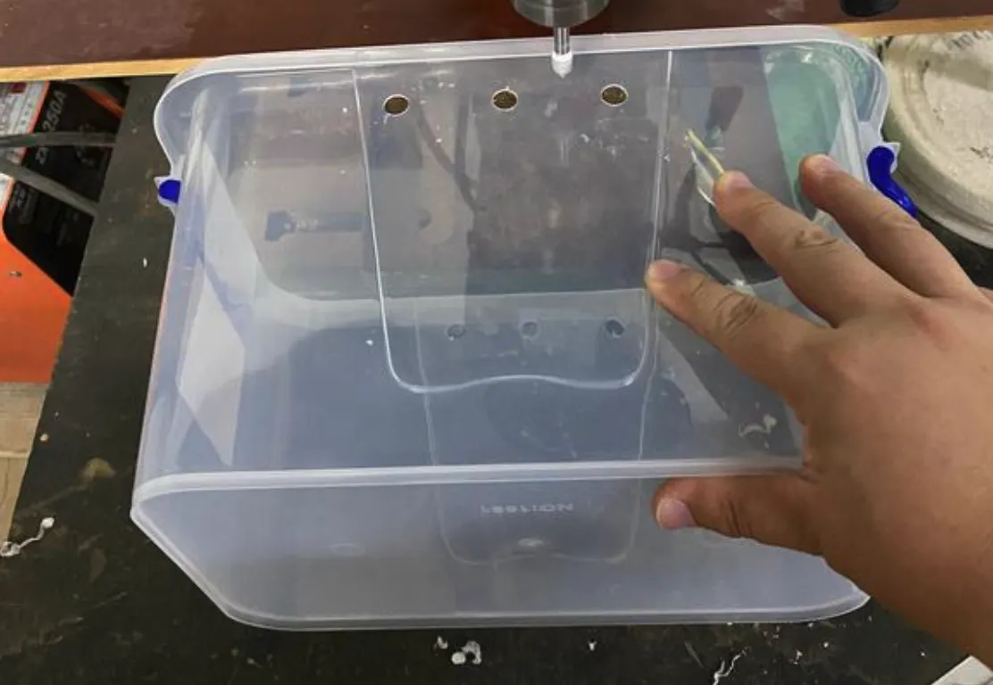 Person adjusting a transparent pet beetle enclosure with ventilation holes on a workbench